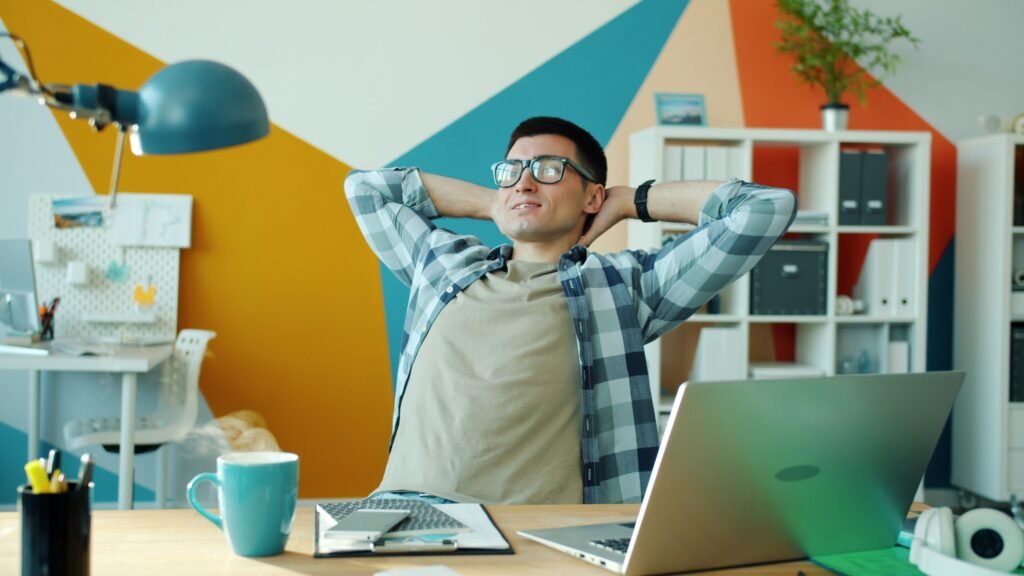 Young man relaxing in modern office with hands behind head, enjoying a break.
